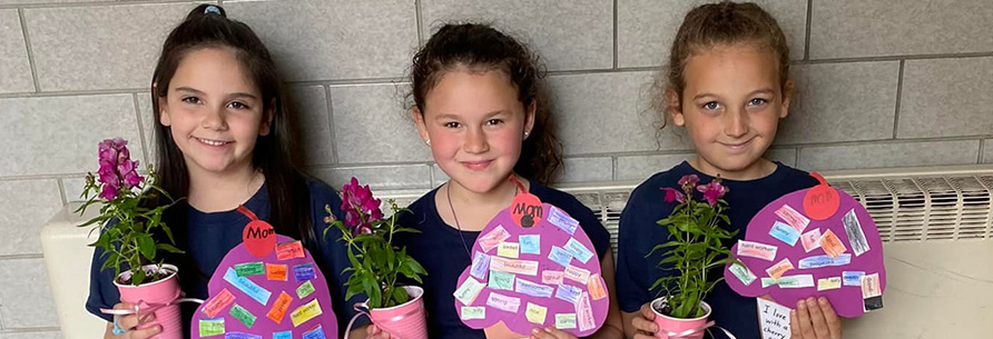 Three girls proudly holding Mother's Day gifts