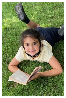 Young girl outside smiling and looking up from book 